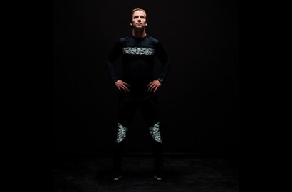 Mann steht in der Dunkelheit, bekleidet mit Shirt und Hose, beleuchtet von 3M Scotchlite Black Stretch Reflective.