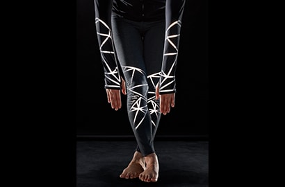 Sportliche Frau nach vorne gebeugt, trägt Sportbekleidung mit leuchtendem 3M Scotchlite C790 Carbon Black Stretch Reflective Material.