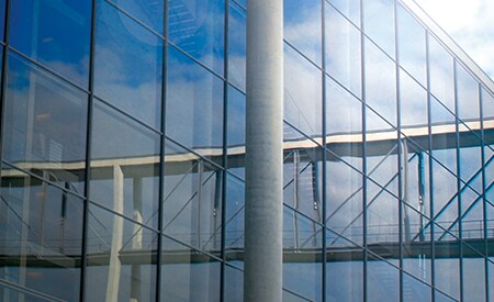 Großes, verglastes Gebäude, in dem sich blauer Himmel und Wolken spiegeln
