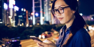Eine Frau blickt vor der Skyline einer Stadt auf ihr Smartphone
