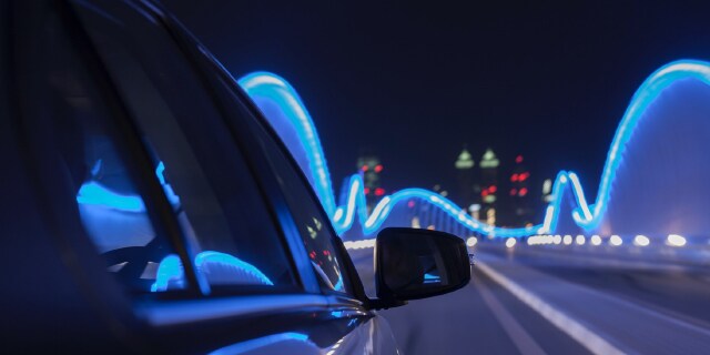Ein Elektrofahrzeug fährt nachts in einer Stadt. Hell erleuchtete Stadt im Vordergrund.