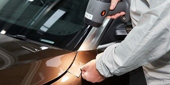 Mann überprüft die Übereinstimmung eines Farbmusters mit der Autolackierungsfarbe mit der 3M Tageslichtlampe II 
