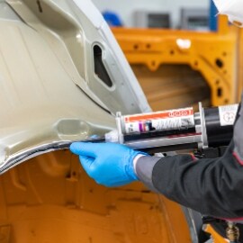 Techniker beim Auftragen von Klebstoff auf das Karosserieteil