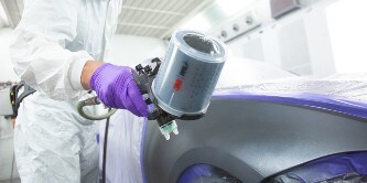Ein Lackierer lackiert eine Auto-Oberfläche mit der 3M Hochleistungslackierpistole
