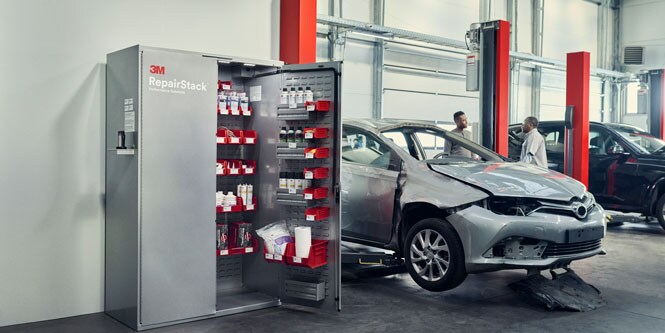 Zwei Personen sprechen neben beschädigten Fahrzeug und offenem 3M™ RepairStack™ Schrank.
