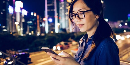 Eine Frau benutzt ihr Mobilgerät in einer Stadt bei Nacht.
