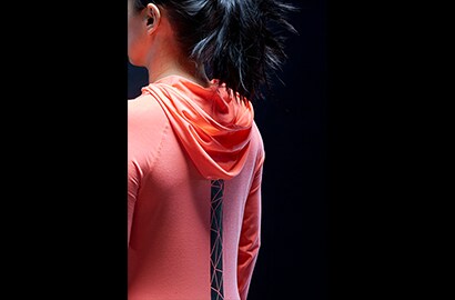 Frau steht in der Dunkelheit in pinkfarbenem Hoodie mit einem 3M Scotchlite Black Stretch Reflective Streifen auf dem Rücken.
