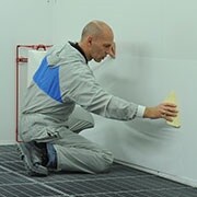 Mann bringt die Dirt Trap Kabinenschutzfolie an einer Wand mit einem Spachtel an