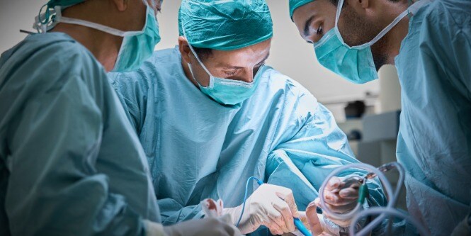 drei Chirurgen beim Operieren einer Patientin mit Brustimplantat
