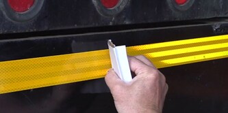 Person, die Konturmarkierung an einem LKW anbringt
