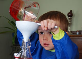 2-year-old William uses a funnel to pour liquid into a bottle to create a tornado in a bottle.