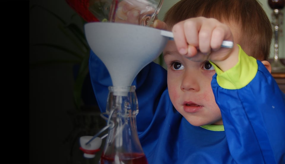 2-year-old William uses a funnel to pour liquid into a bottle to create a tornado in a bottle.