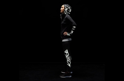 Frau steht in der Dunkelheit bekleidet mit Jacke und Hose, beleuchtet von 3M Scotchlite Black Stretch Reflective.