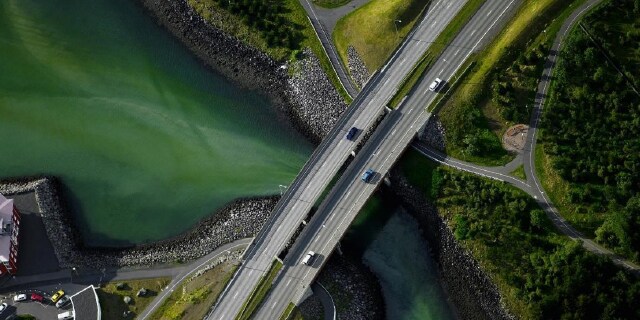 Luftaufnahme von elektrifizierten Fahrzeugen mit hoher Reichweite beim Überqueren einer Brücke auf einer Landstraße.