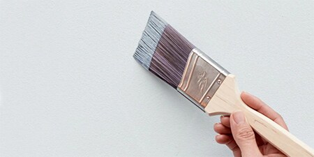 Eine Person, die eine Wand mit der Grundfarbe streicht, um Muster oder Formen hinzuzufügen
