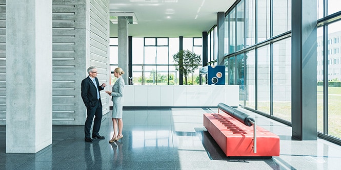 Lobby eines modernen Bürogebäudes mit zwei Geschäftsleuten, die sich unterhalten
