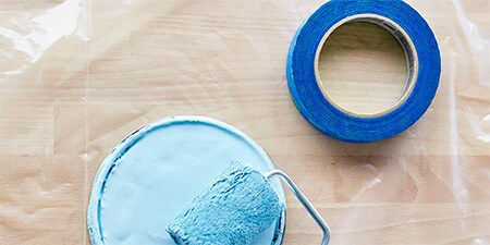 Farbdeckel, Farbrolle und Pinsel auf einer 3M-Abdeckfolie zum Schutz eines Holzbodens
