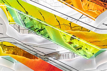 Wände und Rolltreppen eines Einkaufszentrums, mit farbigen 3M Dichroic Glasdesignfolien.
