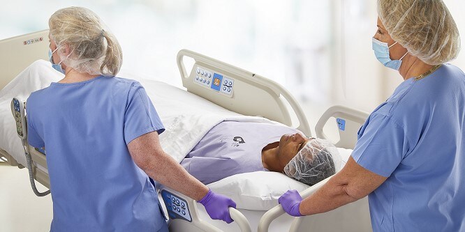 Das Bild zeigt medizinisches Fachpersonal das einen Patienten auf einem Krankenbett transportiert 

