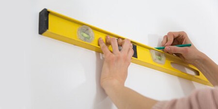 Bild, das eine Person zeigt, die mit einer Wasserwaage Bereiche an einer Wand markiert
