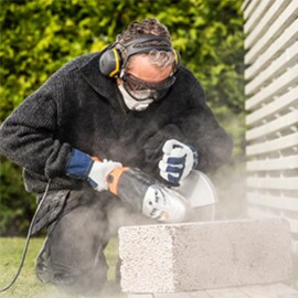 Profi, der eine Betonblock abschleift. Er ist vollständig mit PSA ausgestattet.