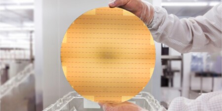 Hände halten einen goldfarbenen Halbleiter-Wafer
