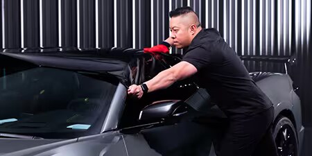 Verarbeiter, der die Folie auf dem Dach eines Fahrzeugs anbringt.
