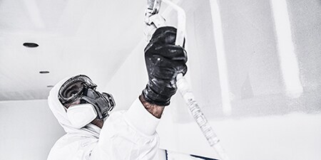Professioneller Dekorateur streicht eine Decke und trägt dabei vollständige PSA von 3M
