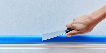Hände, die mit einem Spachtel oder einem Kittmesser das Klebeband richtig andrücken
