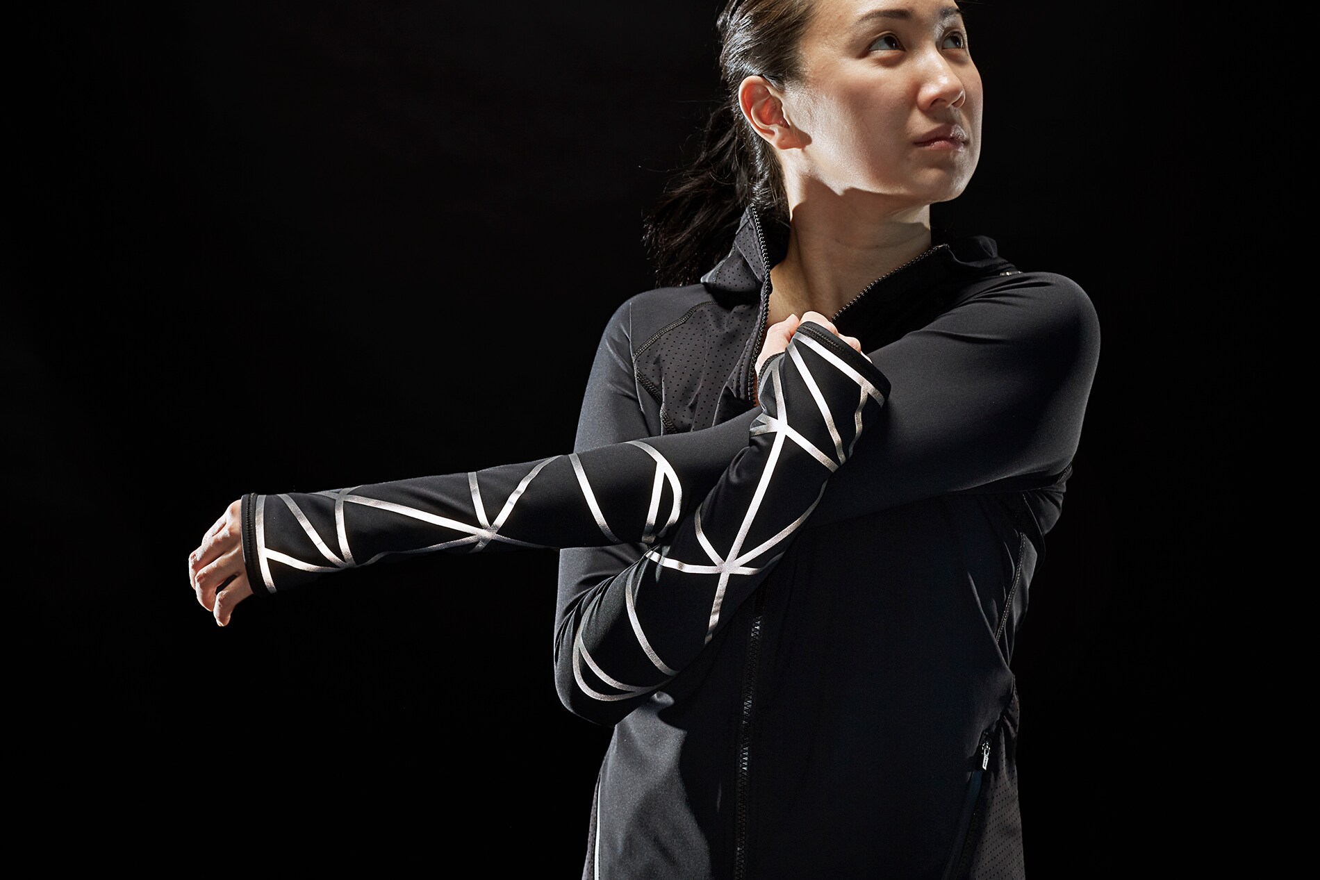Frau streckt Arme und trägt Jacke und Hose, beleuchtet von 3M Scotchlite Black Stretch Reflective.
