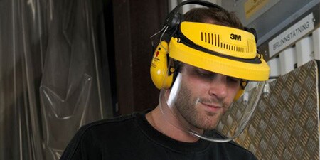 Ein Mann trägt ein Visier mit angebrachtem Kapselgehörschutz in industrieller Umgebung
