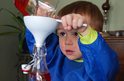 2-year-old William uses a funnel to pour liquid into a bottle to create a tornado in a bottle.