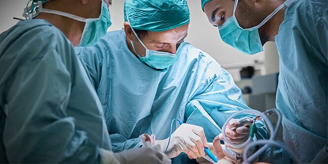 Drei Chirurgen beim Operieren einer Patientin mit Brustimplantat
