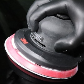Nahaufnahme einer Hand in einem schwarzen Handschuh, die einen 3M™ Elektro- und Druckluft-Exzenterschleifer hält 