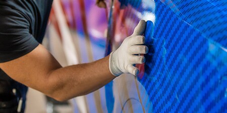 Person, die eine blaue Folie auf einem Fahrzeug anbringt
