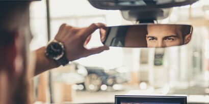 Fahrer betrachtet sein Spiegelbild in einem Autorückspiegel
