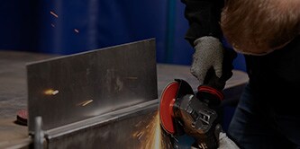 Arbeiter, der mit einer Scotch-Brite™ HD-Vliesscheibe eine Metalloberfläche schleift
