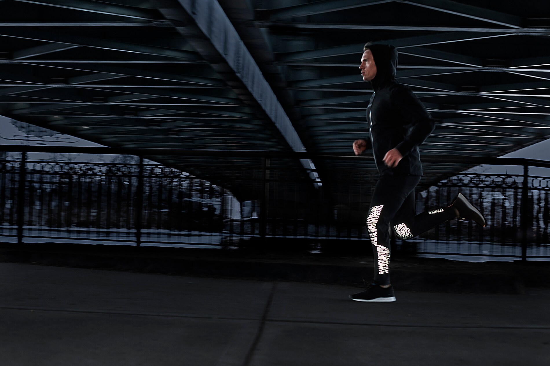 Mann läuft unter einer Stadtbrücke im Dämmerlicht in Lauftights, beleuchtet von 3M Scotchlite Black Stretch Reflective.