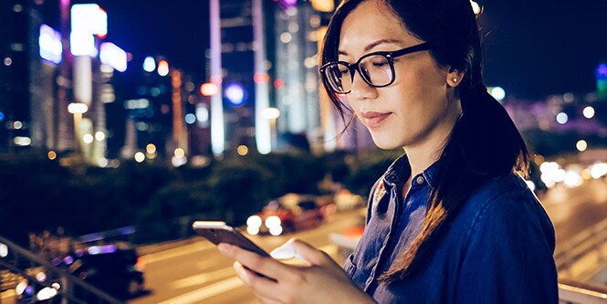Bild einer Frau, die ihr mobiles Gerät in einer Stadt bei Nacht benutzt.

