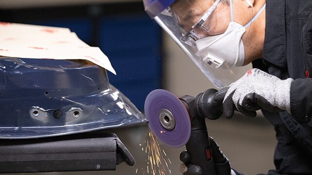 Arbeiter, der mit Schutzausrüstung eine 3M Schleifscheibe auf Metall einsetzt.

