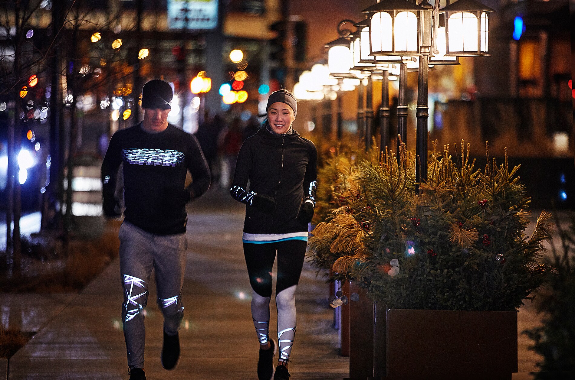Mann und Frau laufen in Stadtbeleuchtung in Laufausstattung, beleuchtet von 3M Scotchlite Black Stretch Reflective.