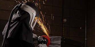 Arbeiter mit Schutzmaske schleift mit Scotch-Brite™ HD-Vliesscheibe eine Metalloberfläche
