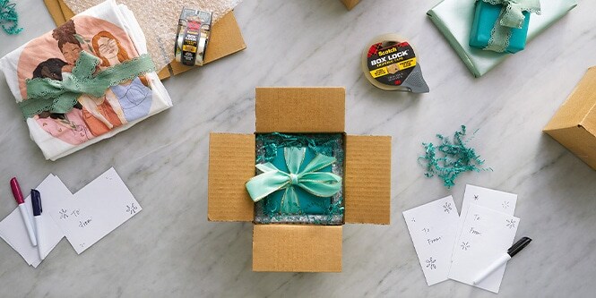 Das Bild zeigt ein Paket mit einem Geschenk neben einem Scotch Box Lock Verpackungsband
