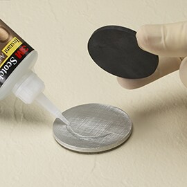 Erfahren Sie mehr über Schritt 2, „Auswahl der Substrate und Materialien“, unter „3M ASPEC-Methode“. Bild eines Cyanacrylat-Klebstoffs, der zwischen einer runden Scheibe aus Metall und einer aus Schaumstoff aufgetragen wird