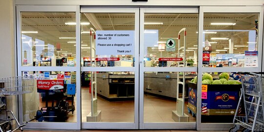 Bild eines Supermarkteinganges mit Sticker auf der Glastüre 
