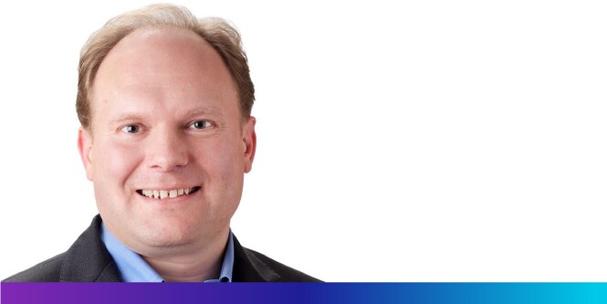 Ein Mann lächelt vor einem weißen Hintergrund.
