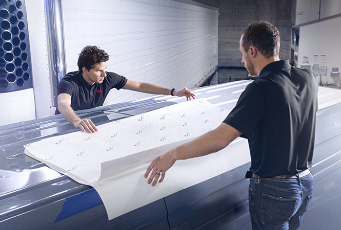 Techniker bringen in einer Servicewerkstatt 3M Folie auf dem Dach eines Fahrzeugs an.

