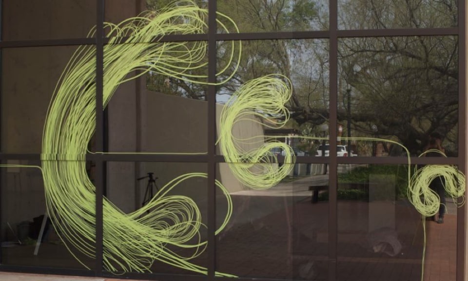 Karine Fellini’s artwork made from Scotch Performance Masking Tape. Green lines of tape create colorful artwork on a window.