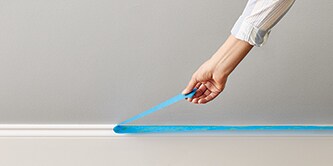 Person beim Abziehen von ScotchBlue™ Abdeckband von einer Fußleiste

