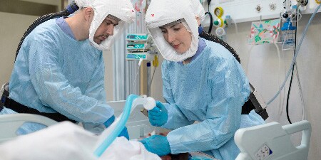 Bild zeigt 2 Mitarbeiter im Gesundheitswesen mit PSA, die sich um einen Patienten kümmern
